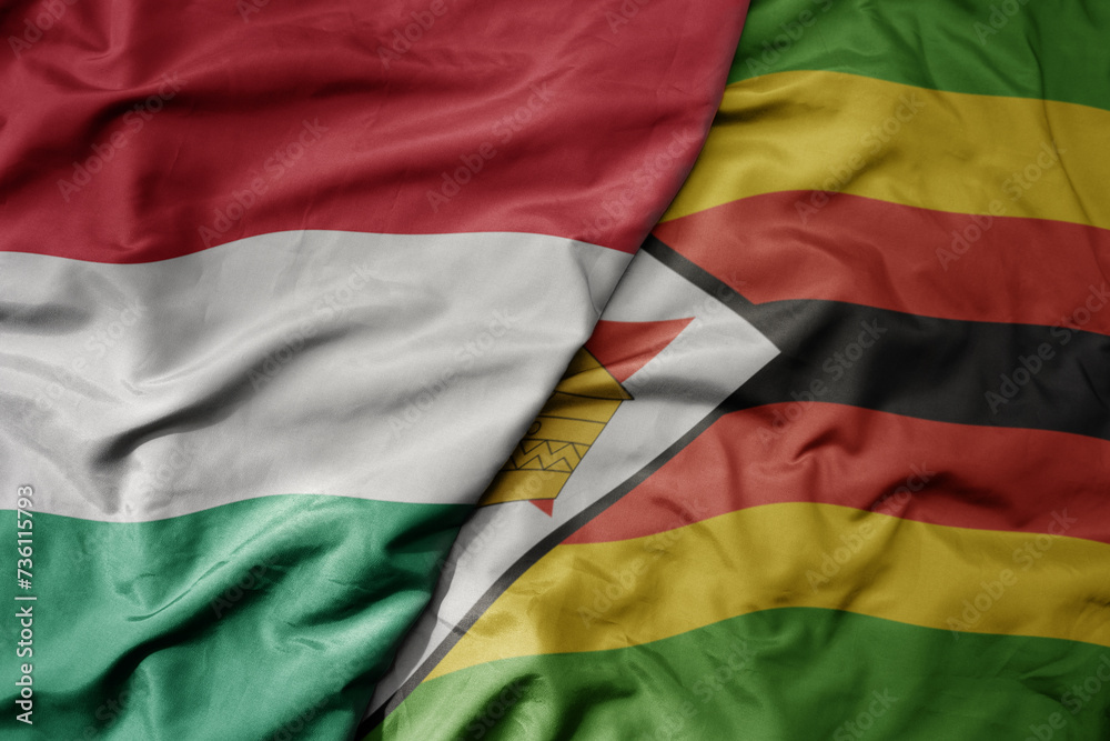 big waving national colorful flag of zimbabwe and national flag of hungary .