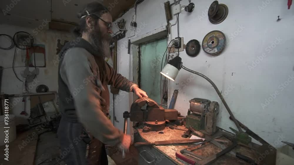 a man with a beard in torn clothes sharpens metal a man with a beard in torn clothes sharpens metal