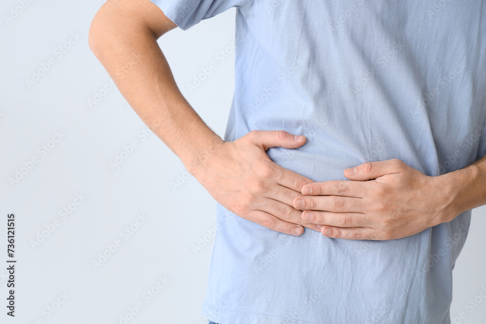 Young man suffering from side pain on light background Young man suffering from side pain on light background