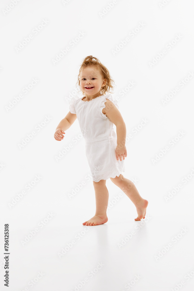 Firs step. Full length portrait of little girl in cute dress have fun and running against white studio background. Concept of childhood, motherhood, life, carefree, birth. Copy space for ad Firs step. Full length portrait of little girl in cute dress have fun and running against white studio background. Concept of childhood, motherhood, life, carefree, birth. Copy space for ad