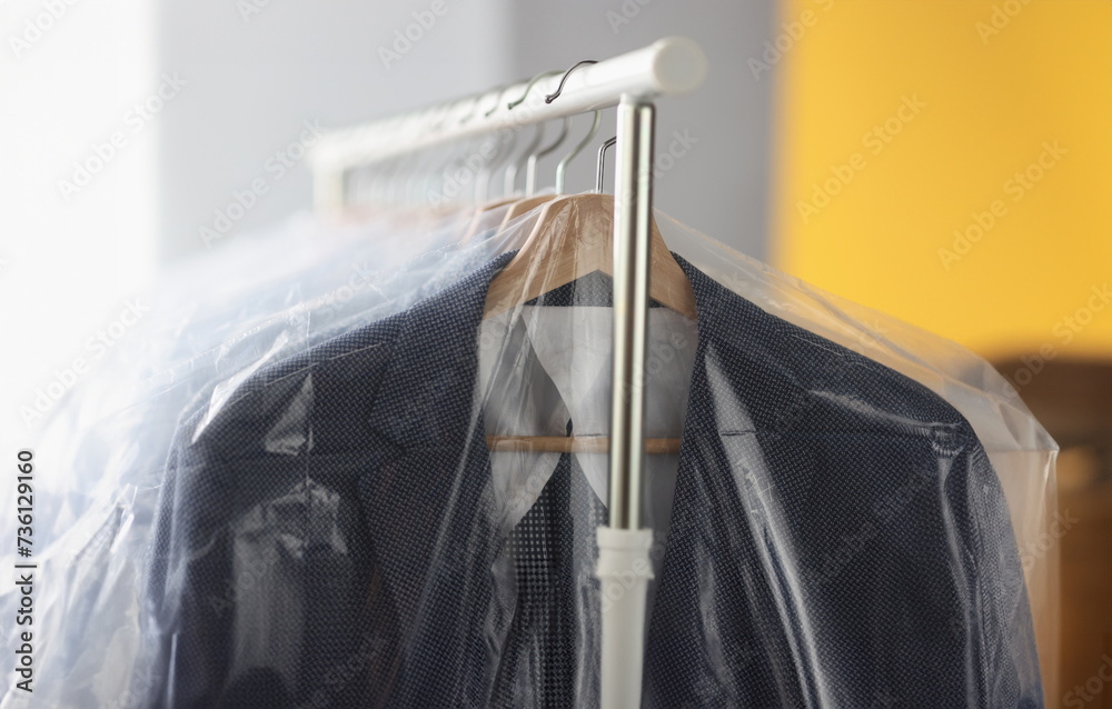 Clothes in plastic bags hanging on hanger in laundry closeup. Dry cleaning service concept
