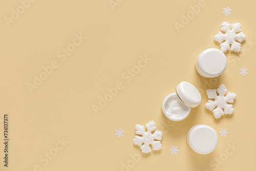 Jars of cream with decorative snowflakes on pale yellow background