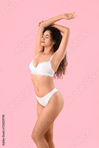 Beautiful young African-American woman with stretch marks on her body against pink background