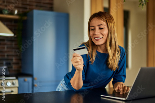 A smiling blonde woman, using and reading information from the credit card.,