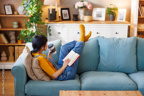 Woman drinking coffee and reading a book while relaxing at home photo