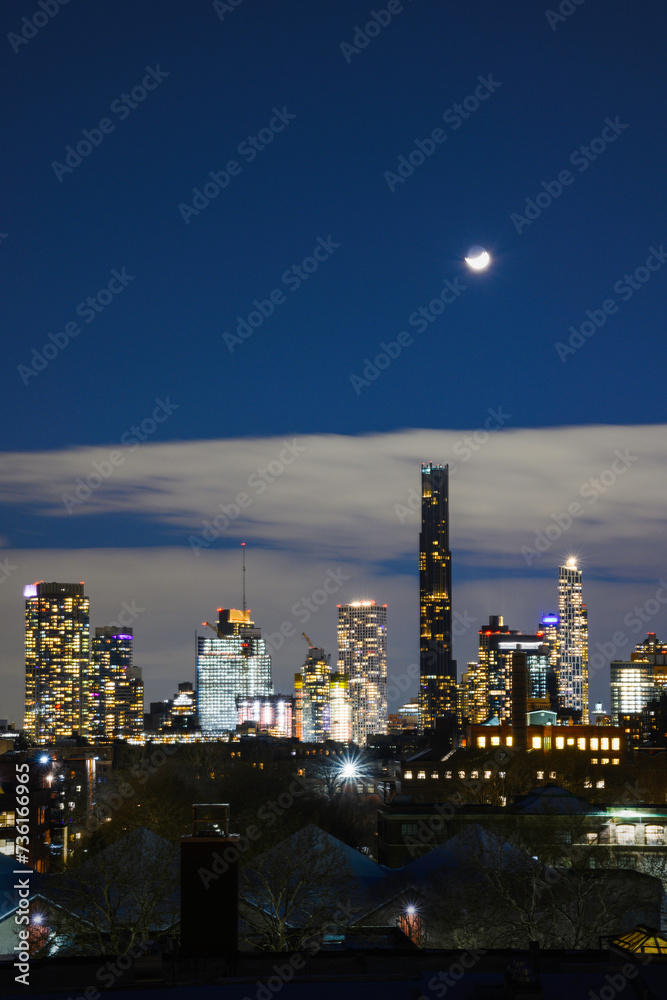 Naklejka premium Moonrise over New York City Skyline, a tranquil nostalgic twilight landscape over Brooklyn rooftops on a cloudy winter night, USA