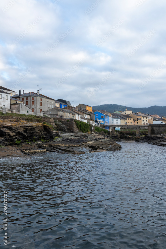 tranquil coastal town with colorful buildings, calm sea, rocky shores, under a cloudy yet bright sky