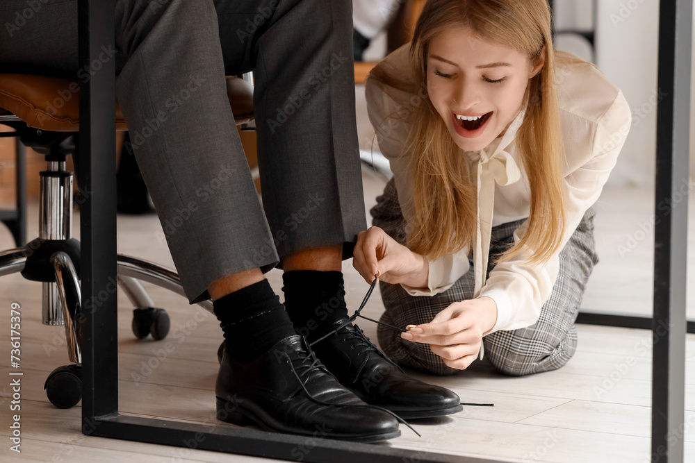Young woman tying her colleague's shoe laces in office. April Fools' Day celebration