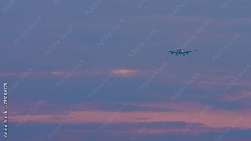 Long shot of a jet passenger plane approaching landing in a gloomy sky. Sunset or dawn, airplane in the sky. Airliner descent, arrival. Travel concept