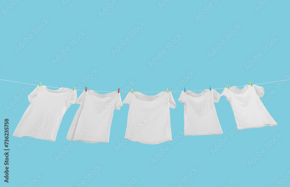 T-shirts drying on washing line against light blue background, low angle view