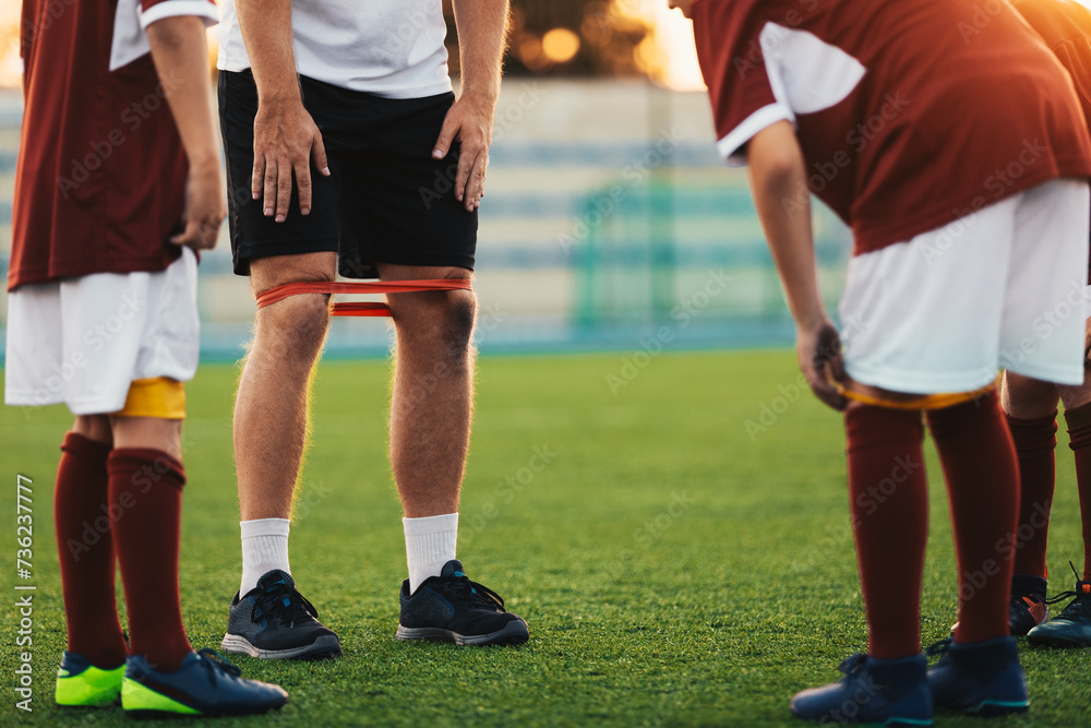 Group of School Kids at Fitness Class With Coach. Boys in Soccer Clothes Using Stretching Bands in Practice. Fitness Training for Youth Football Team Group of School Kids at Fitness Class With Coach. Boys in Soccer Clothes Using Stretching Bands in Practice. Fitness Training for Youth Football Team