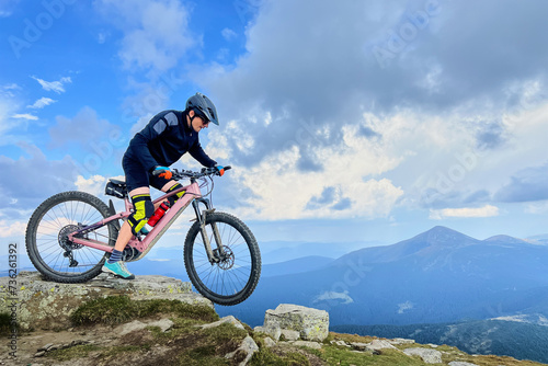 Cyclist man riding electric mountain bike outdoors. Male tourist biking along grassy trail in the mountains, wearing helmet. Concept of sport, active leisure and nature.