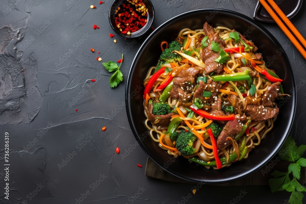 Top view of stir fried beef and veggie noodles in a black bowl on a slate background with space to copy Top view of stir fried beef and veggie noodles in a black bowl on a slate background with space to copy