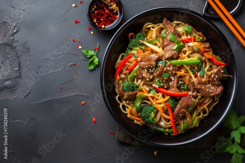 Top view of stir fried beef and veggie noodles in a black bowl on a slate background with space to copy