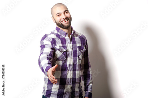 Nice to meet you! Young handsome bearded man in casual plaid shirt holding hand to welcome you while standing against white background.