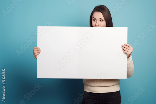A girl or woman standing in a studio holding a blank sign for your own message of protest, sale, promotion or other against a colour, coloured, colorama backdrop green blue photo