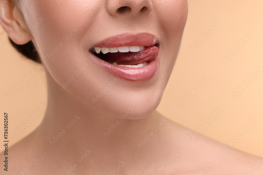 Fototapeta premium Woman with beautiful lips licking her teeth on beige background, closeup