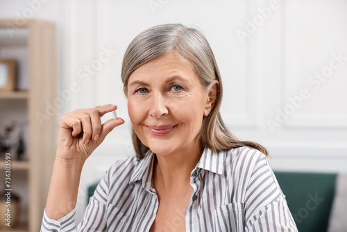 Menopause, hormone replacement therapy. Happy woman holding pill at home photo