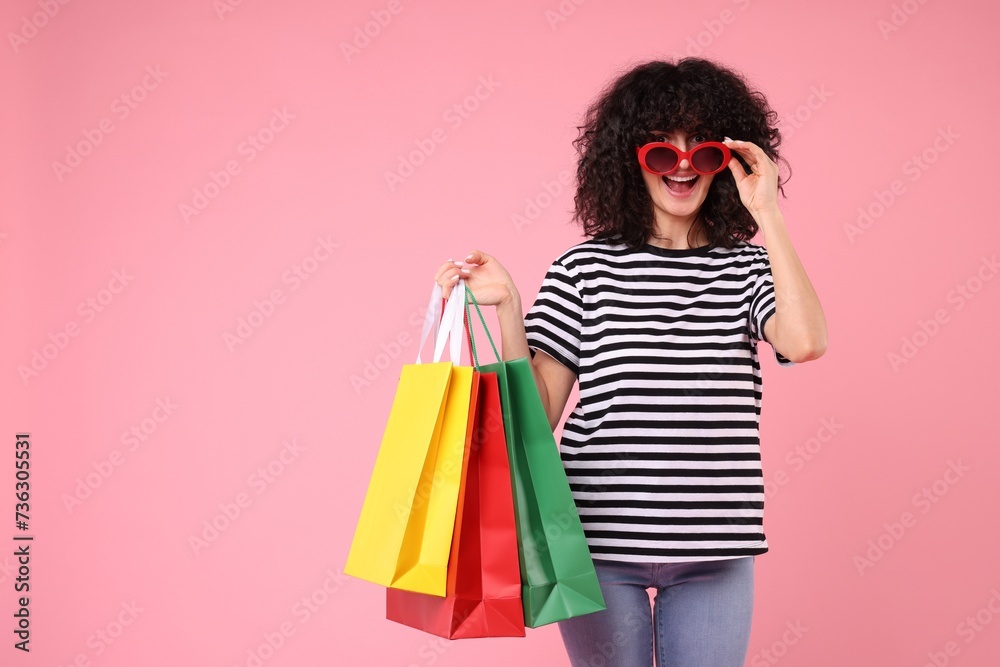 Happy young woman with shopping bags and stylish sunglasses on pink background. Space for text
