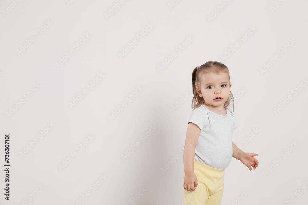 Cute little girl standing near white wall at home, space for text Cute little girl standing near white wall at home, space for text