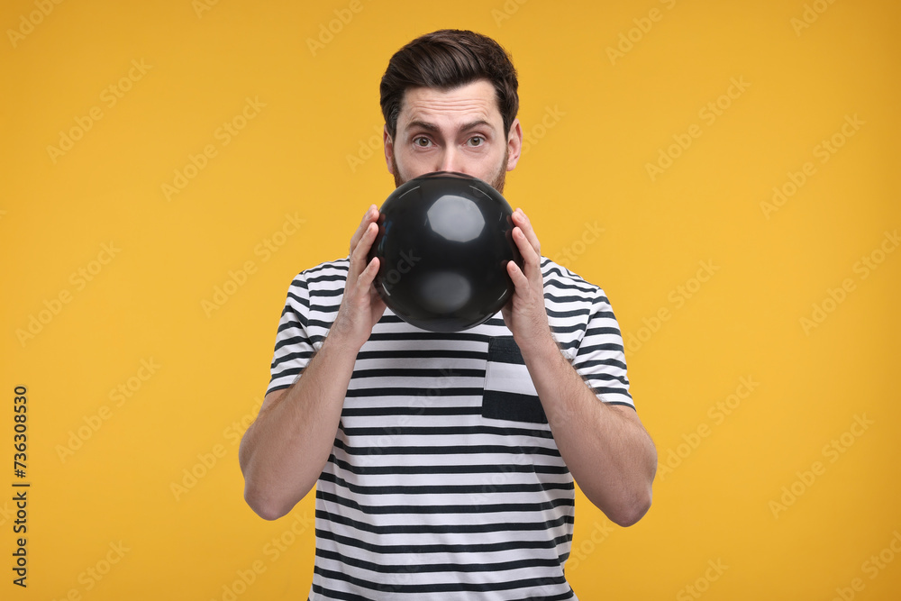 Man inflating black balloon on yellow background Man inflating black balloon on yellow background