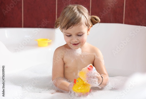 Little girl bathing with toy ducks in tub