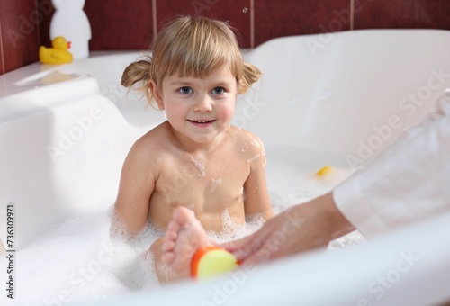 Mother washing her smiling daughter with sponge in bathtub, closeup