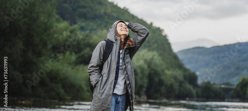 A young woman in a raincoat walking along the bank of a mountain river. Rest travel and relaxation with nature photo