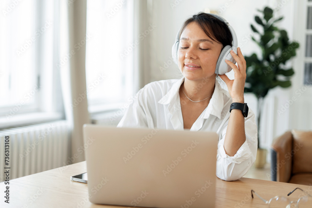 Relaxed woman with headphones enjoying music during a break, experiencing a moment of peace in a bright, cozy workspace. Relaxed woman with headphones enjoying music during a break, experiencing a moment of peace in a bright, cozy workspace.