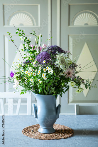 Blumenstrauss in einer Vase aus Keramik vor einem SChrank aus Holz. Frühlingsblumen: Kamille, Eustoma, Anemone, Spirea, Allium, Strandflieder, Zweige