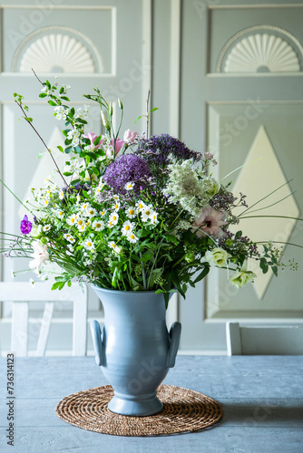 Blumenstrauss in einer Vase aus Keramik vor einem SChrank aus Holz. Frühlingsblumen: Kamille, Eustoma, Anemone, Spirea, Allium, Strandflieder, Zweige