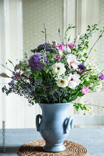 Blumenstrauss in einer Vase aus Keramik vor einer Glastür. Frühlingsblumen: Kamille, Eustoma, Anemone, Spirea, Allium, Strandflieder, Zweige