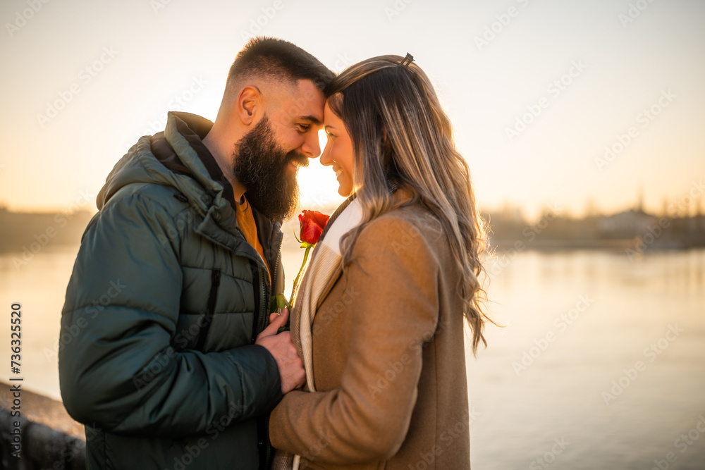 Happy man giving red rose to his woman while they enjoy spending time together on a sunset. Happy man giving red rose to his woman while they enjoy spending time together on a sunset.