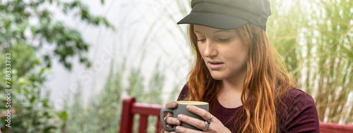 Horizontal banner or template with pensive young redhead woman drinking latte or coffee at caffetteria bar garden - Young woman with red hair and freckles with her head in the clouds - Focus on face photo