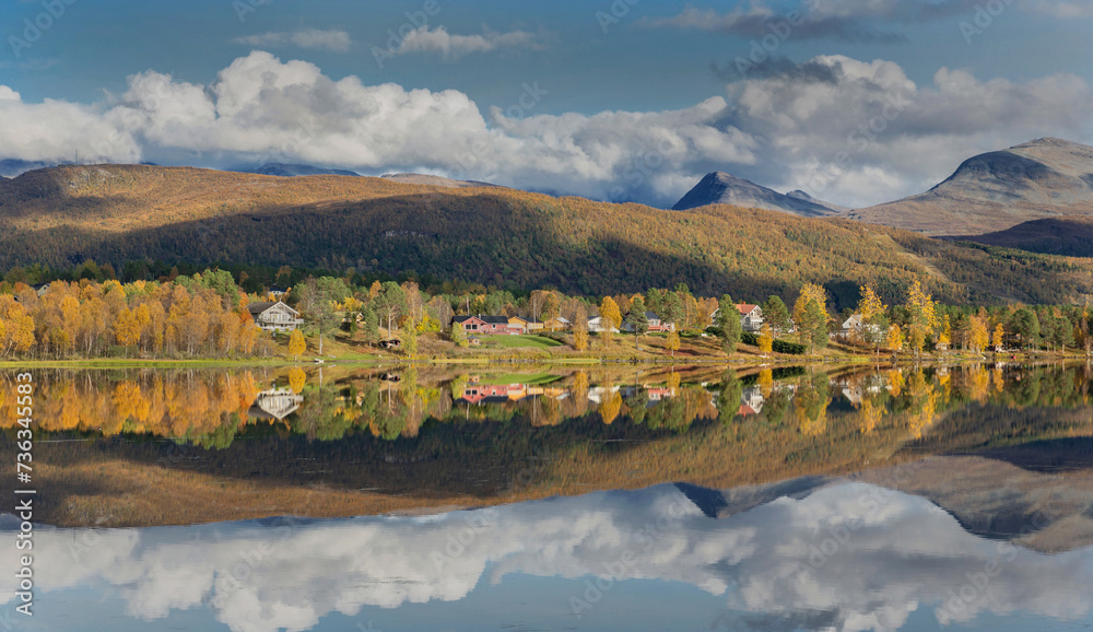 beautiful scenic landscape with mountain and autumnal forest under the sky reflecting in surface of water in Norway..