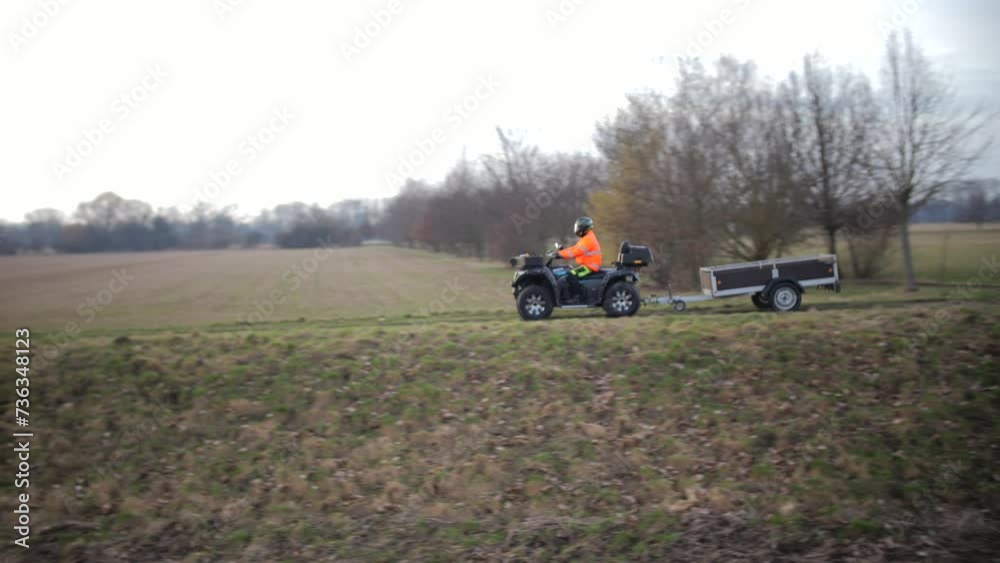 ATV Rider in High Visibility Jacket Towing a Trailer Across a Field ATV Rider in High Visibility Jacket Towing a Trailer Across a Field