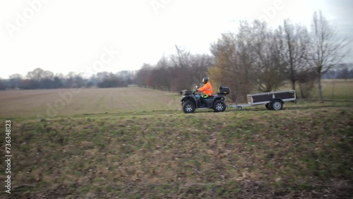 ATV Rider in High Visibility Jacket Towing a Trailer Across a Field