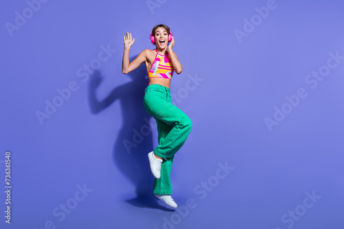 Full body length photo of young lady dj loves music hipster jumping in wireless pink earphones isolated on violet color background