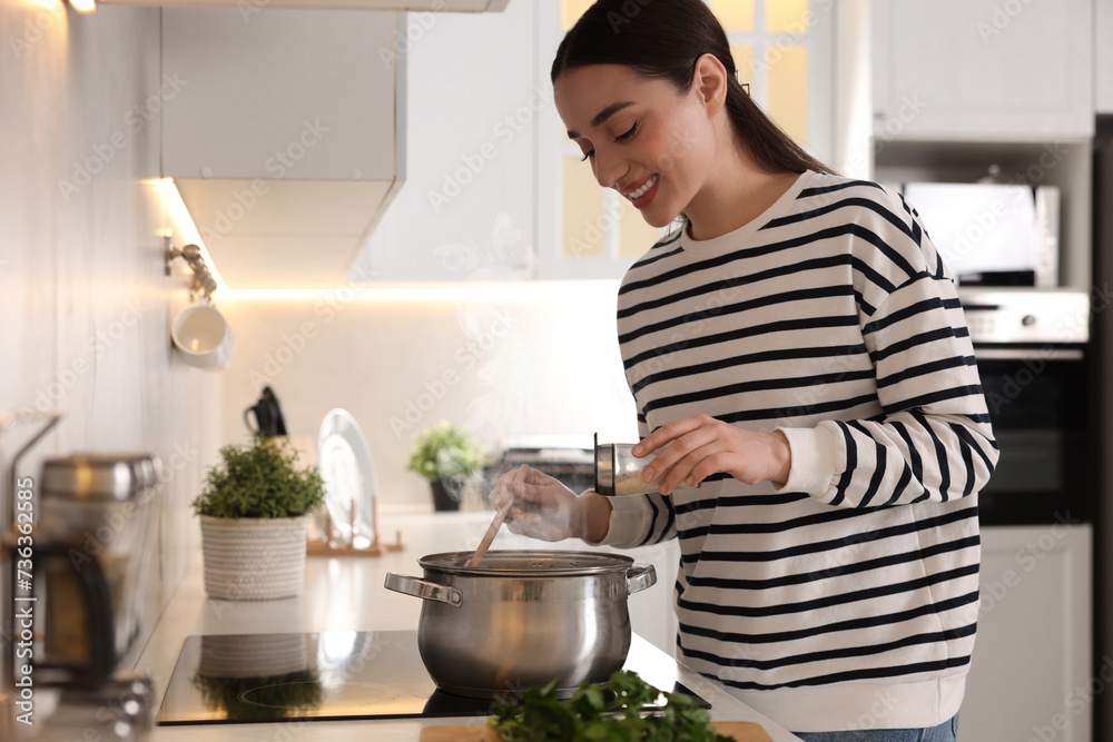 Smiling woman adding spices into pot with soup in kitchen Smiling woman adding spices into pot with soup in kitchen