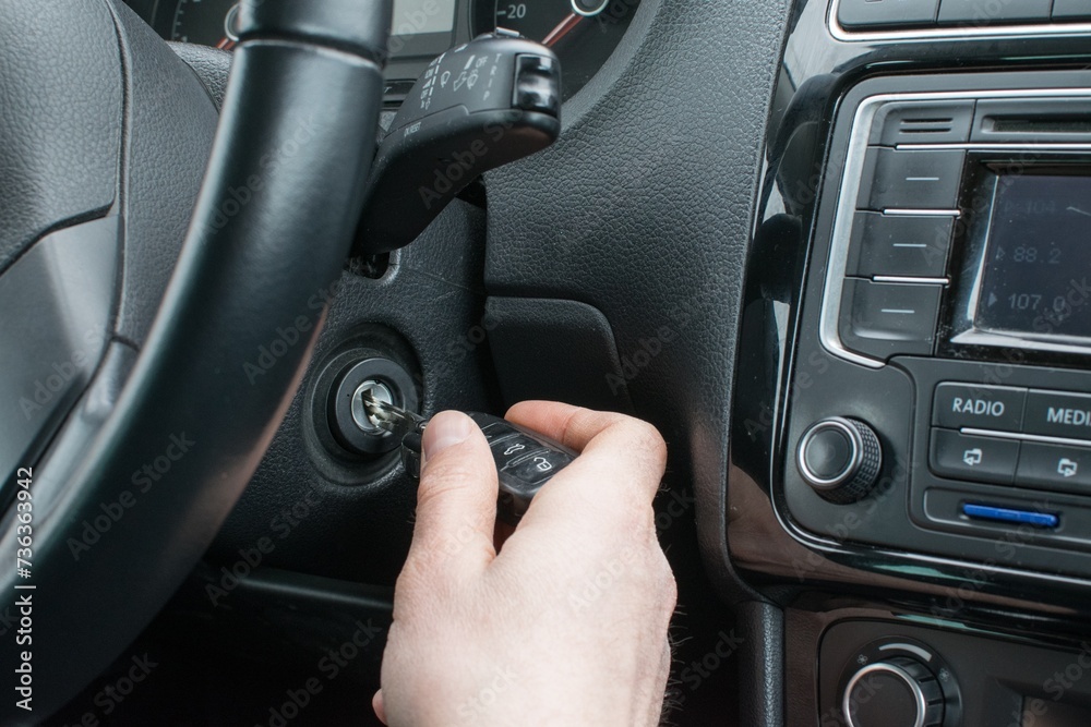 The male driver's hand inserting the key into the ignition lock of the car, on the background of the steering wheel and panel