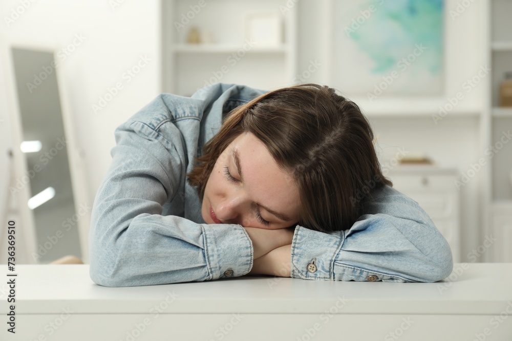 Sad young woman sitting at white table in room Sad young woman sitting at white table in room