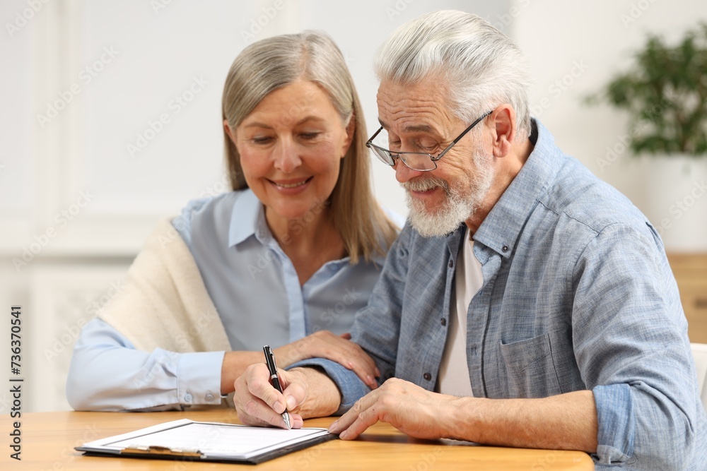 Happy senior couple signing Last Will and Testament indoors Happy senior couple signing Last Will and Testament indoors