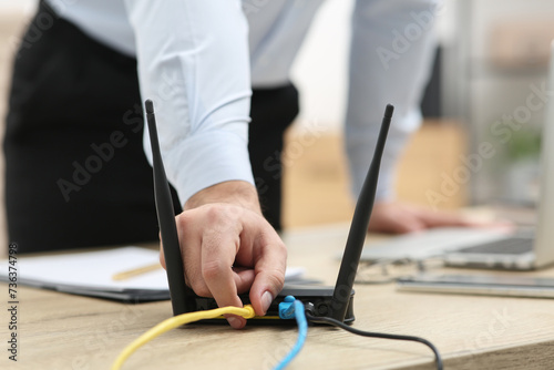 Fotografie Man inserting cable into Wi-Fi router at wooden table indoors, closeup