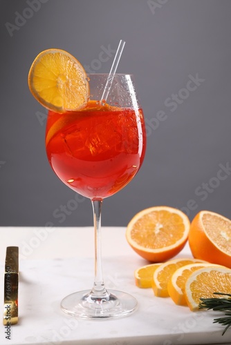 Glass of tasty Aperol spritz cocktail with orange slices on white table against gray background