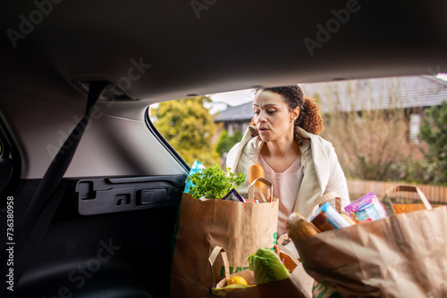 Woman taking groceries out of car trunk