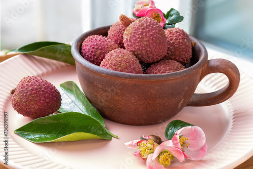 Lychee fruits in rustic ceramic teacup. Litchi Sonn. Flowers of Japanese quince. Tropical fruits. Litchi chinensis