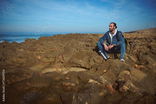 Caucasian young bearded man traveler, sitting alone on the rocky cliff, looking into the distance, enjoying the nature. People. Travel. Active tourism. Copy advertising space © Taras Grebinets