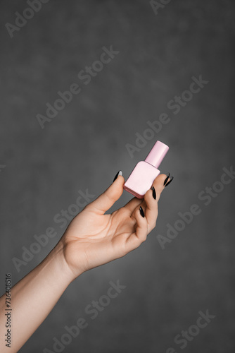 Woman's hand holding pink nail polish bottle against gray background.