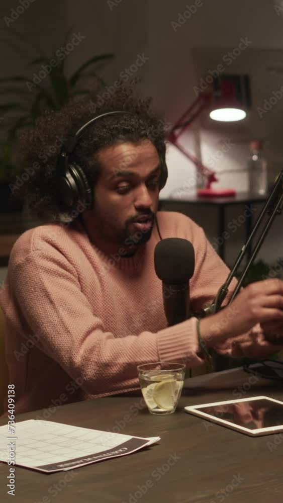 Vertical of Biracial guy visiting dark broadcast studio at nighttime, giving interview during audio podcast recording Vertical of Biracial guy visiting dark broadcast studio at nighttime, giving interview during audio podcast recording