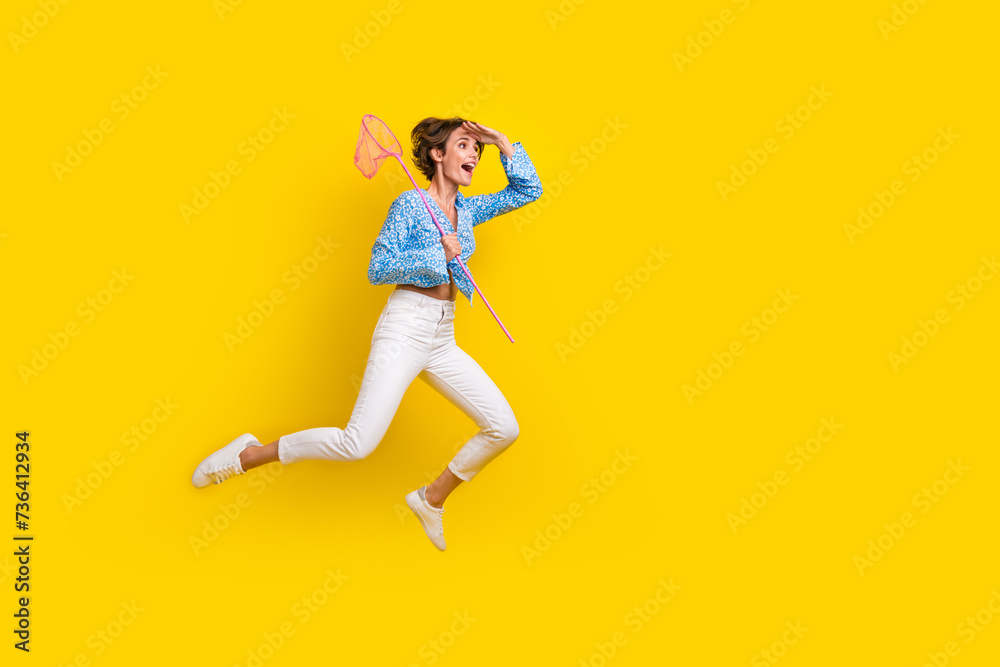 Full size photo of impressed woman wear print blouse flying look empty space hold butterfly net isolated on yellow color background